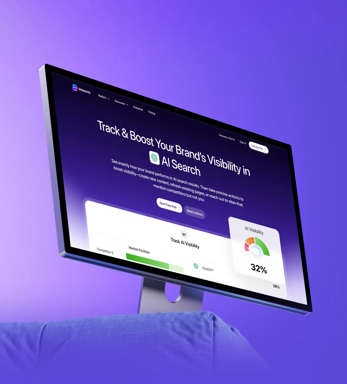 The Writesonic AI visibility homepage on a desktop monitor, standing on a soft purple cushion