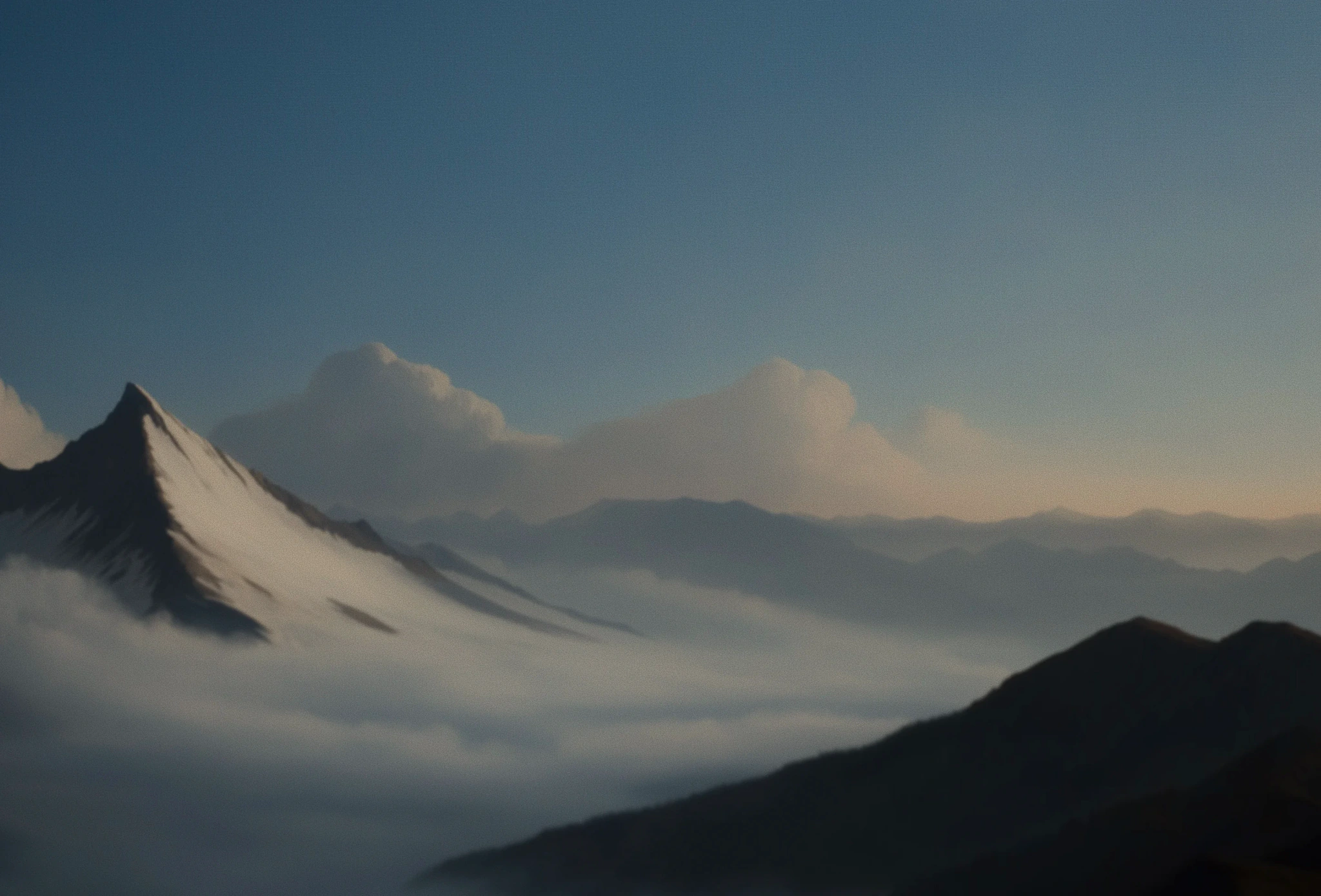 A snow-capped peak rising above a misty mountain range at dusk
